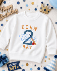 A white sweatshirt with the text "BORN 2 VICK BAT" printed on it, surrounded by birthday decorations such as a crown, confetti, and a birthday hat.