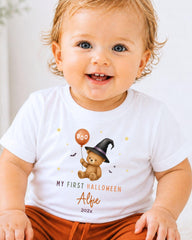 A smiling baby wearing a white t-shirt with a Halloween-themed graphic and text.