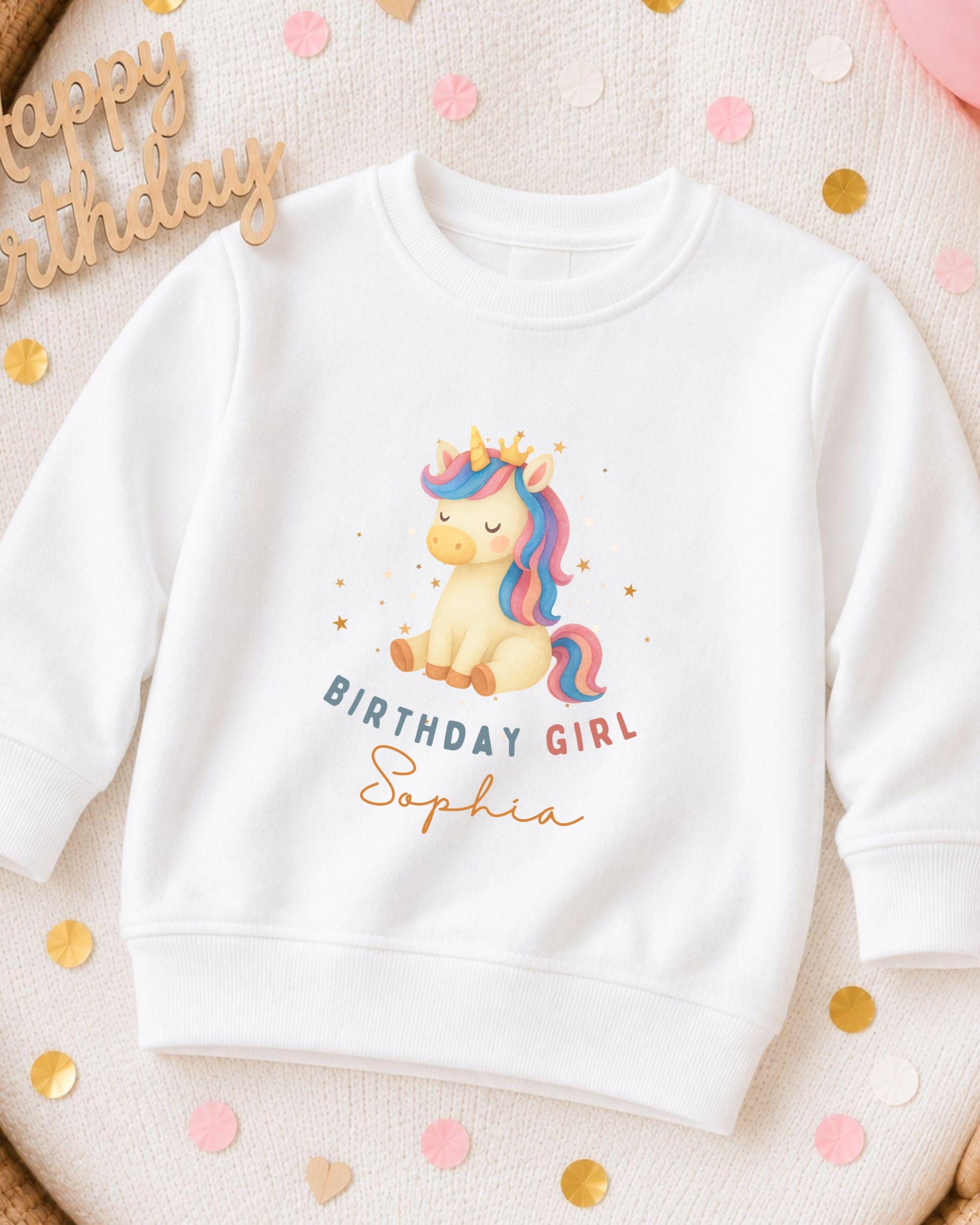 A white sweatshirt with a unicorn graphic and the text "Birthday Girl Sophia" printed on it, surrounded by confetti.