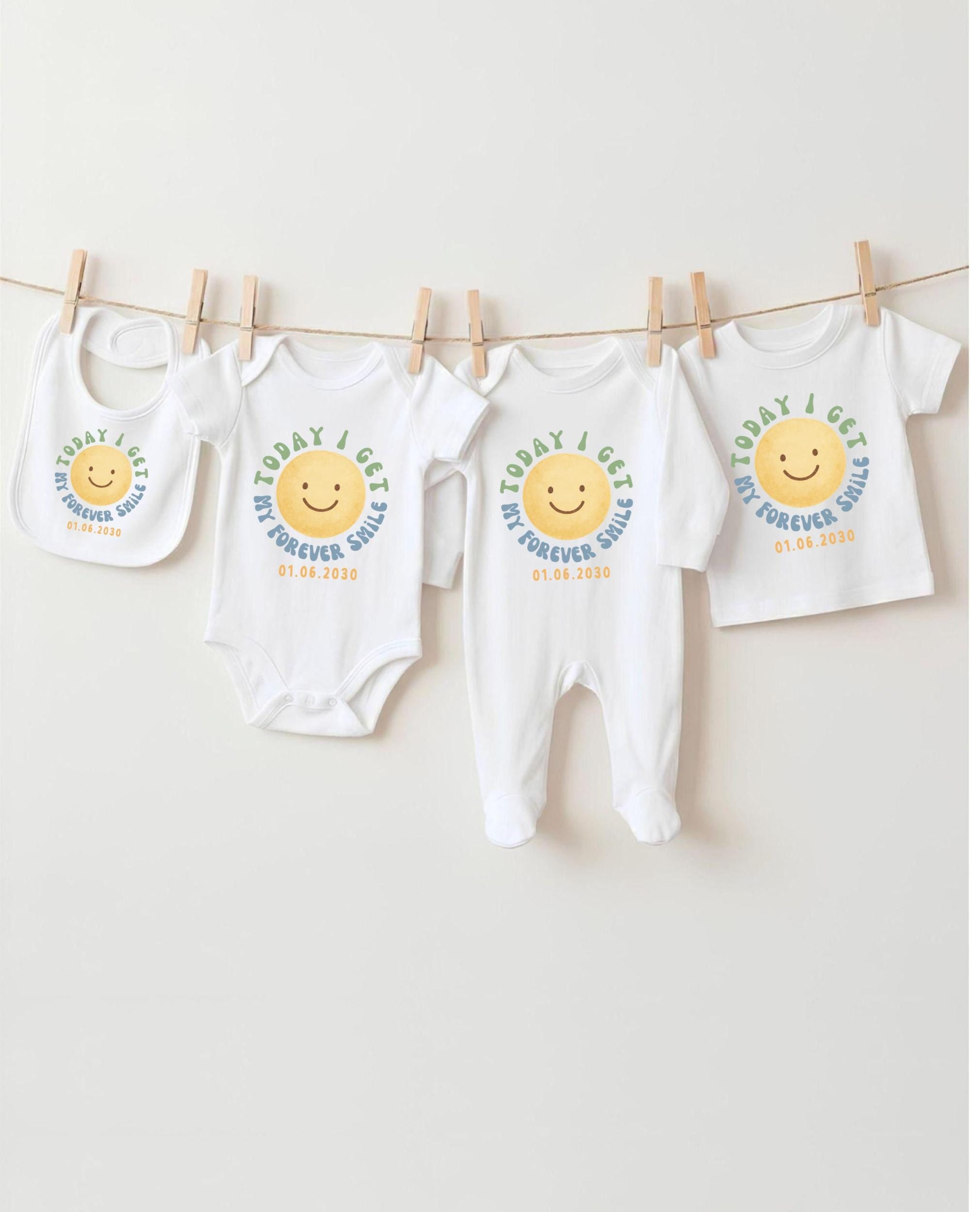 A row of four white baby clothes with a smiley face design, hanging on a clothesline.