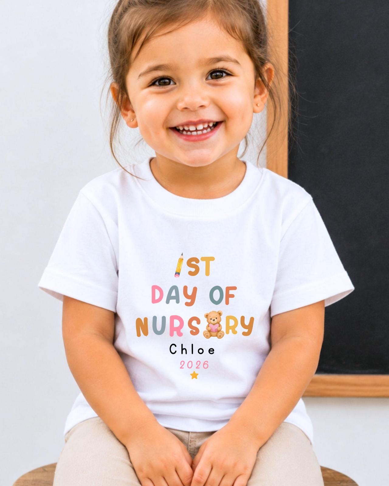 A young girl wearing a white t-shirt with text and a teddy bear graphic, smiling at the camera.