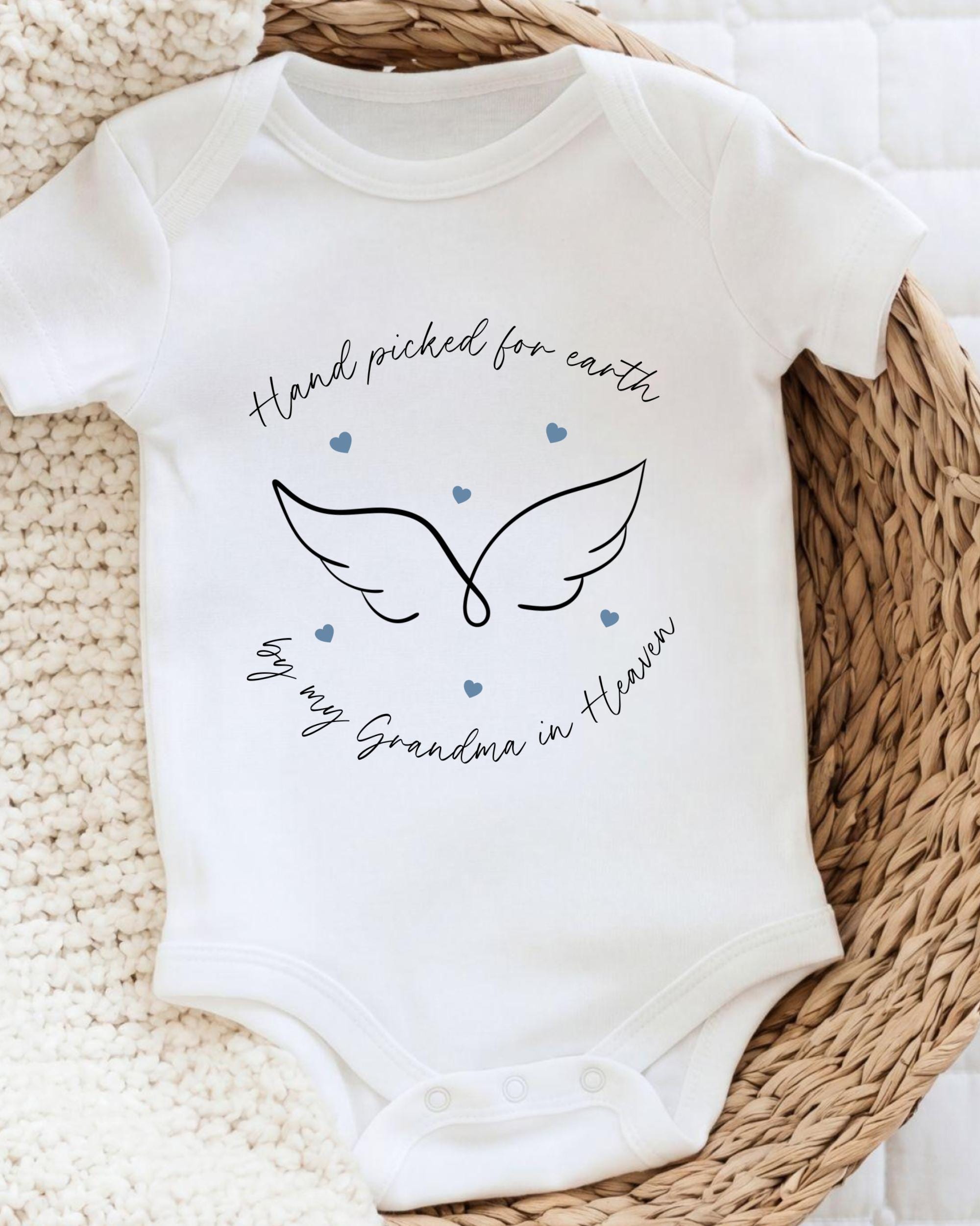 A white baby onesie with a graphic design and text on it, placed on a woven basket.