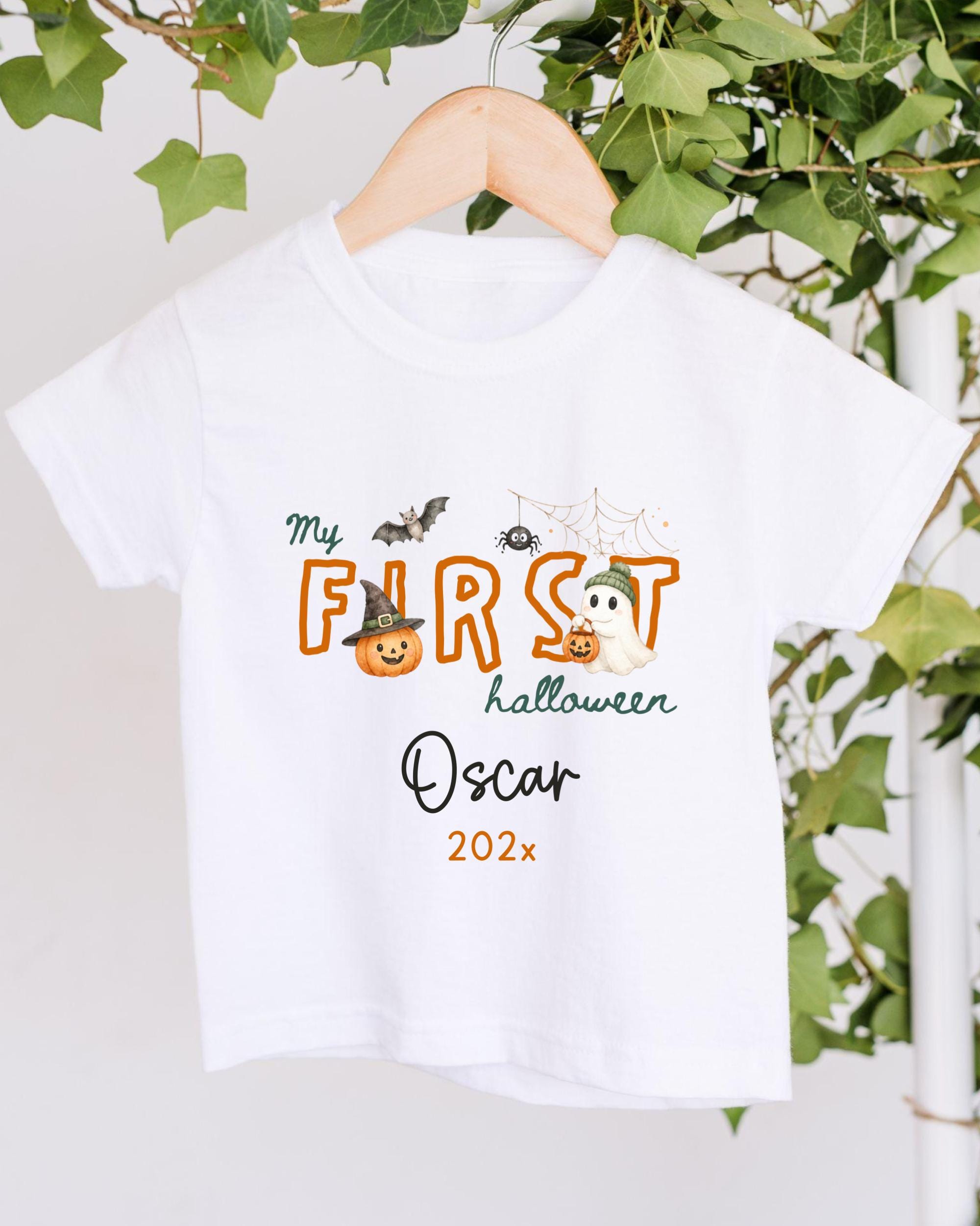 A white t-shirt with a Halloween-themed design hanging on a wooden hanger.