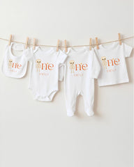 A row of four white baby clothes with the name "Emilly" printed on them, hanging on a clothesline.