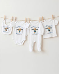 A collection of baby clothes, including onesies and bibs, hanging on a clothesline.