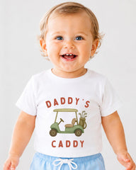 A smiling baby wearing a white t-shirt with a golf cart graphic and the text "DADDY'S CADDY" printed on it.