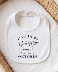 A white bib with text printed on it, placed on a white cloth or blanket.