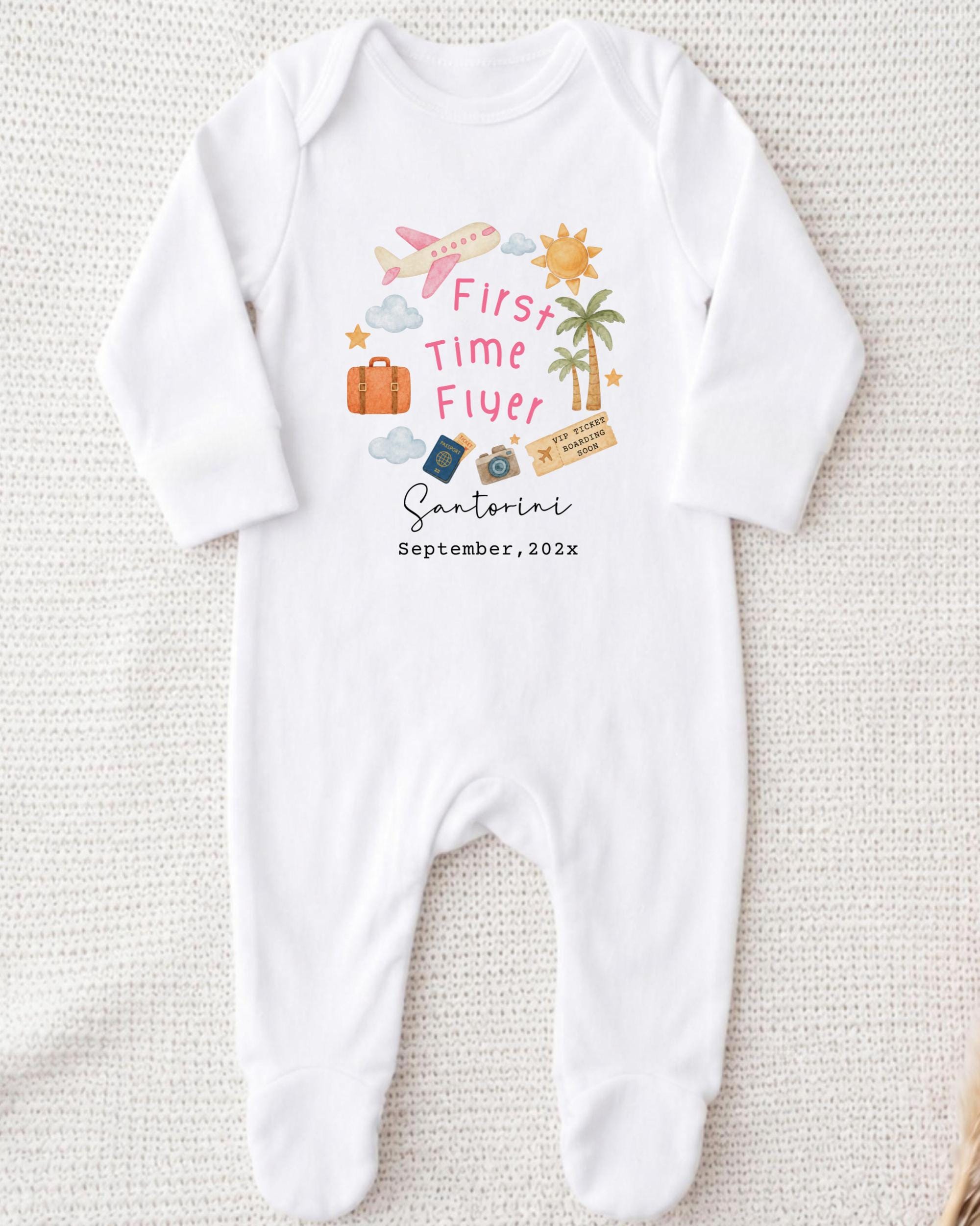 A white onesie with a graphic design on it, featuring various travel-related icons such as a suitcase, a plane, and a palm tree.