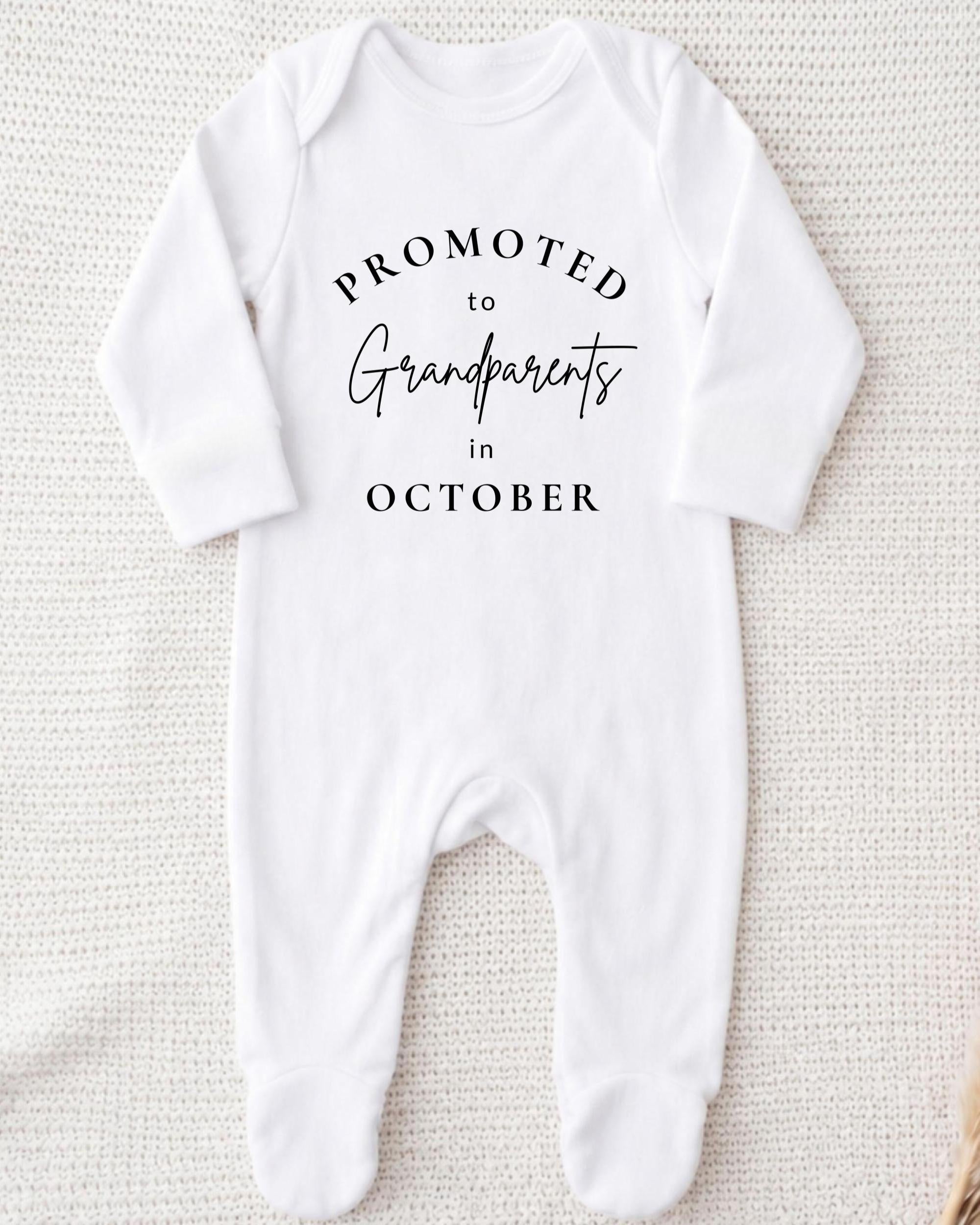 A white onesie with the text "Promoted to Grandparents in October" printed on it.
