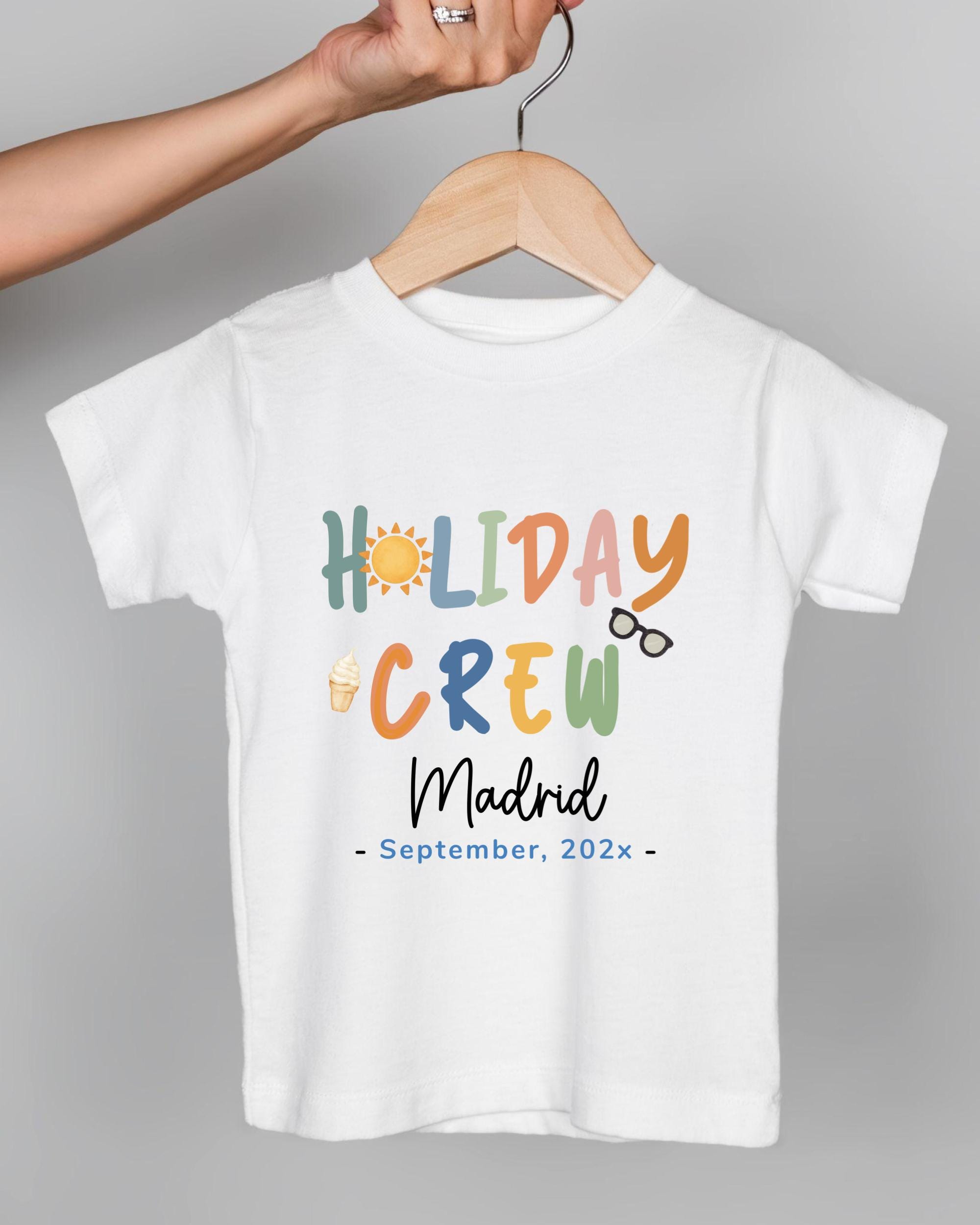 A white t-shirt with colorful text and icons printed on it, hanging on a wooden hanger.