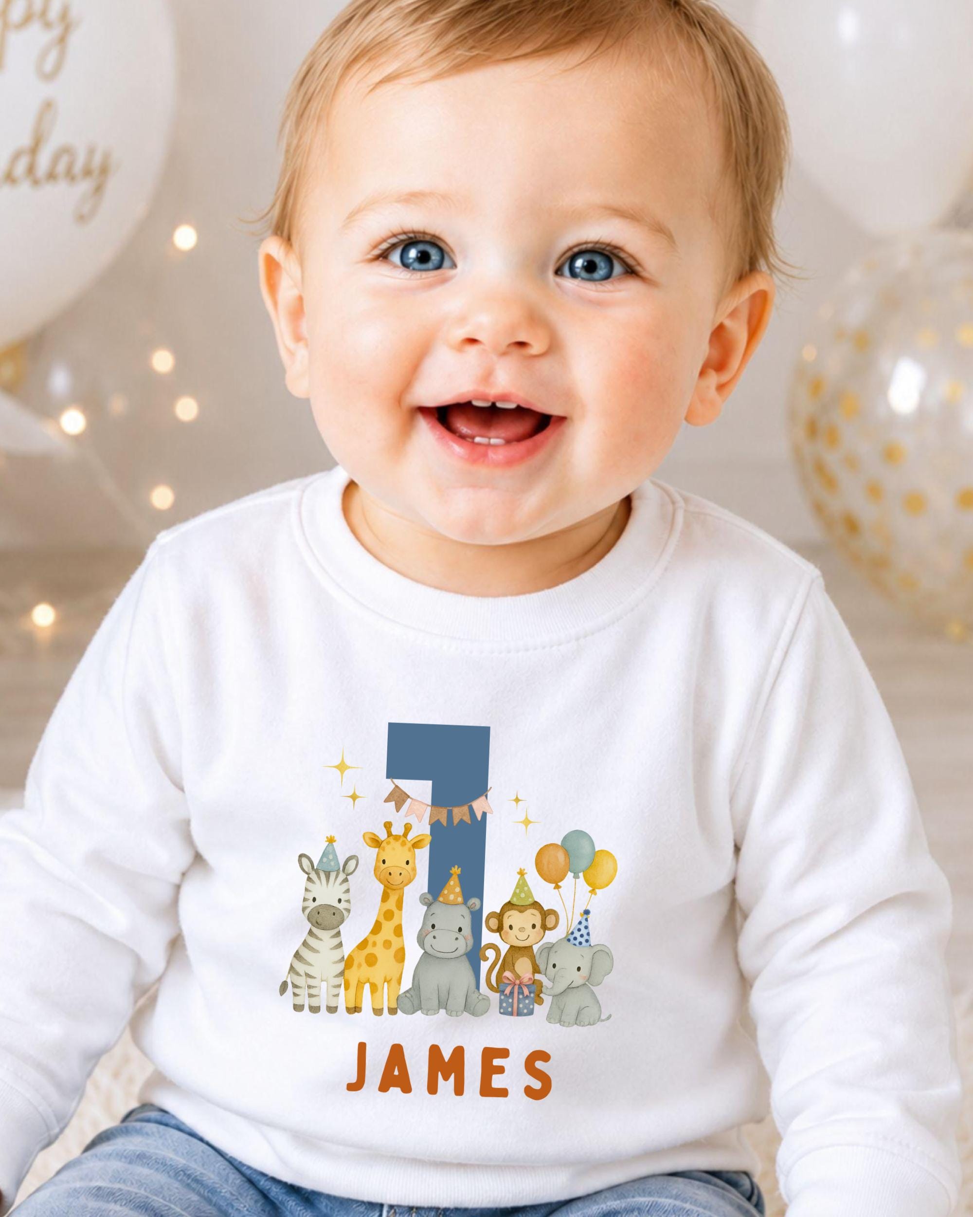 A smiling baby boy wearing a white shirt with a cartoon image of animals and the name "James" printed on it.