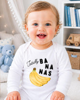 A smiling baby wearing a white onesie with a banana graphic and the text "Totally BANANA" printed on it.