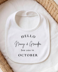 A white bib with the text "Hello Nanny & Grandpa See you in October" printed on it, placed on a white cloth.