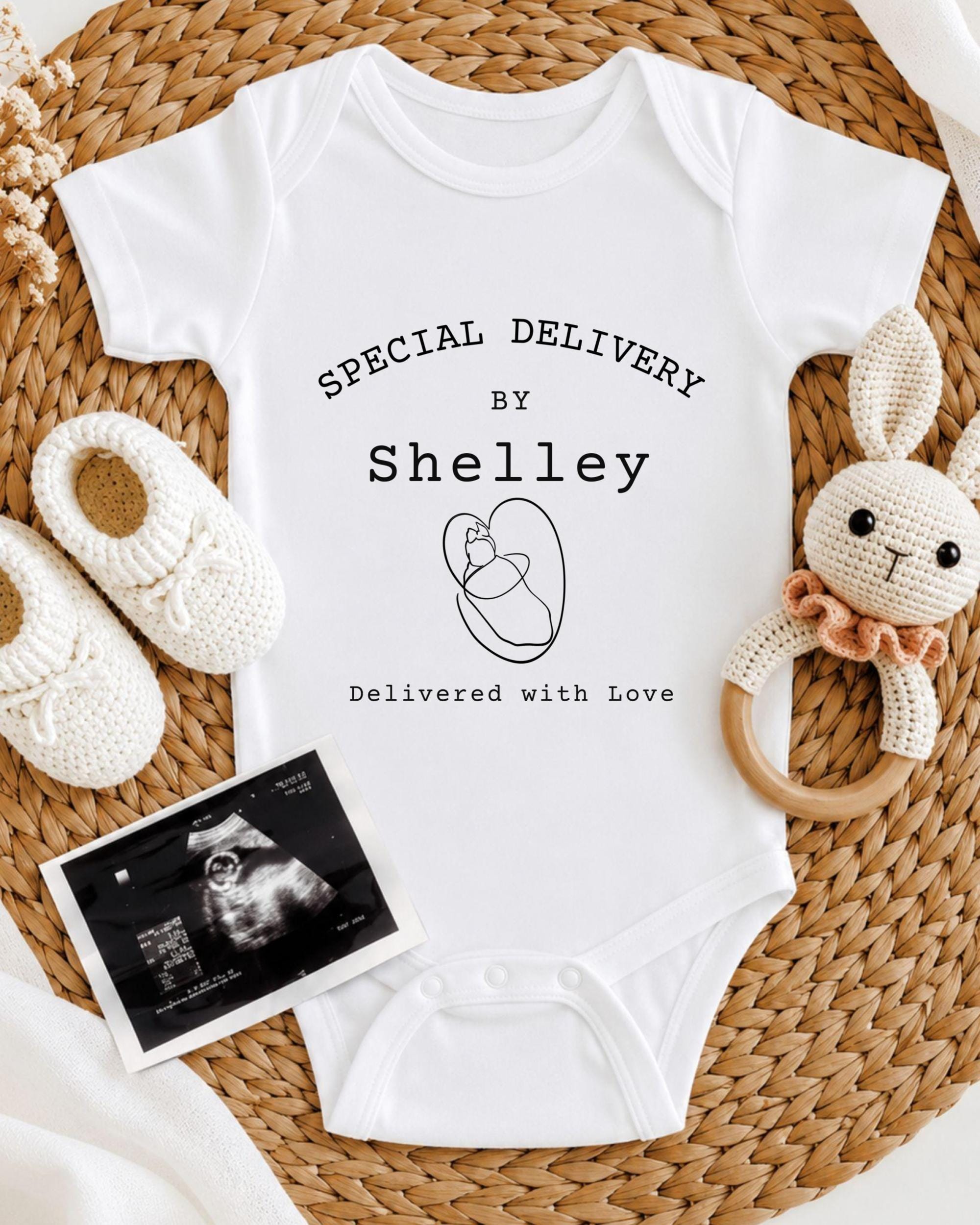 A white baby onesie with text, a crocheted bunny toy, and a black and white photograph of an infant's belly.