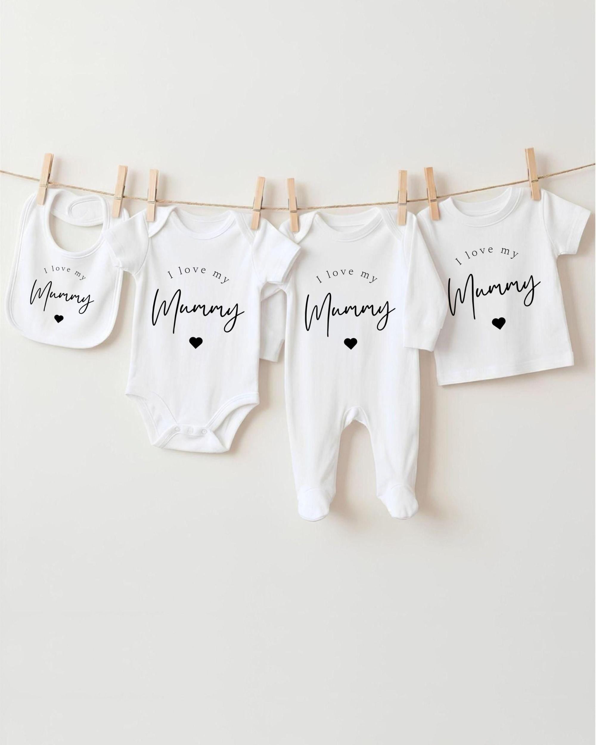 A row of four white baby clothes with the text "I love my Mummy" printed on them, hanging on a clothesline.