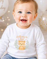 A smiling baby boy wearing a white shirt with a cartoon tiger graphic and the text "Halfway to One Teddy" printed on it.