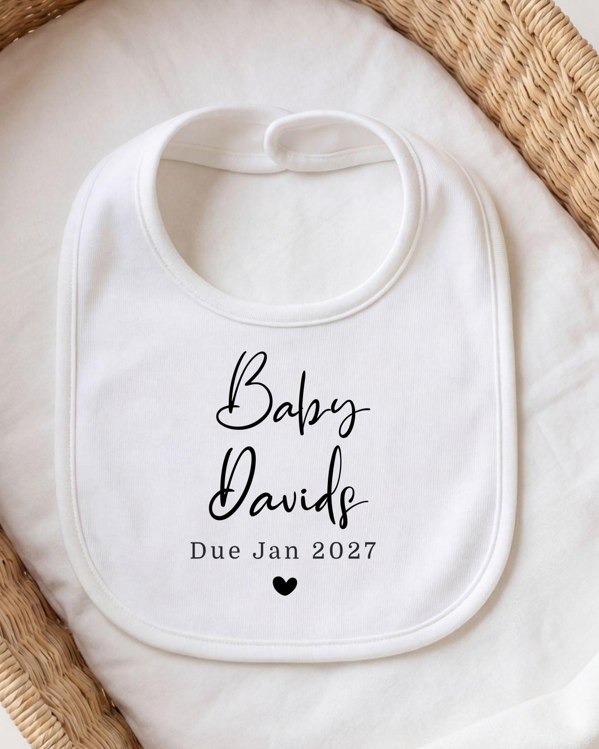 A white bib with black text and a heart symbol, placed on a white cloth.