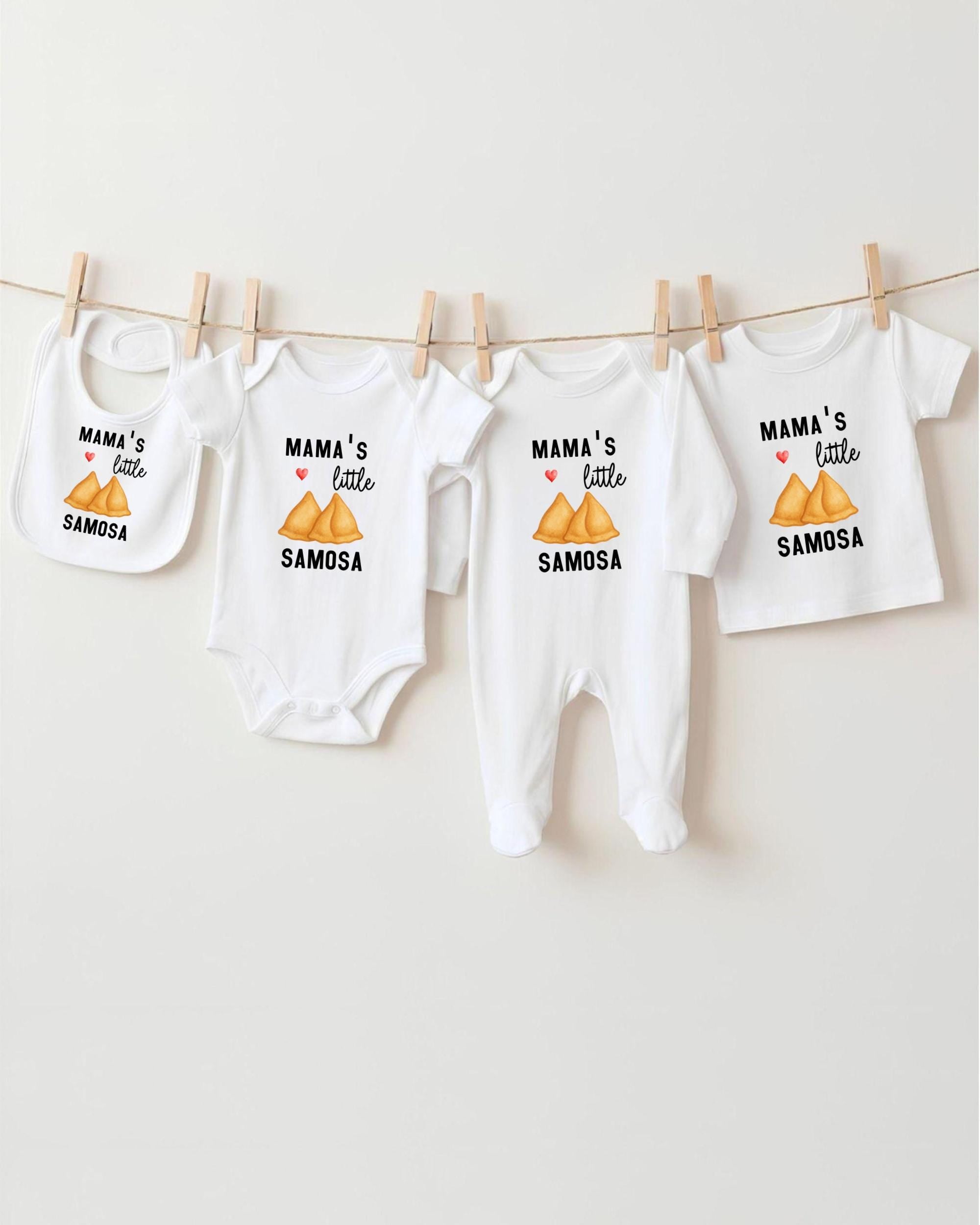 A row of four white baby clothes with the text "MAMA'S LITTLE SAMOSA" printed on them, hanging on a clothesline.