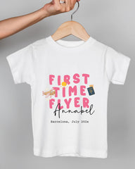 A white t-shirt with pink text and an illustration of an airplane, along with the text "FIRST TIME FLYER Annabel Barcelona, July 202x".