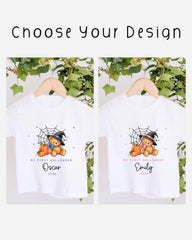 two white t-shirts with a teddy bear and a spider web design, hanging on a wooden hanger. The text on the t-shirts reads "My first Halloween Oscar 2020" and "My first Halloween Emily 2020", indicating the names of the babies.
