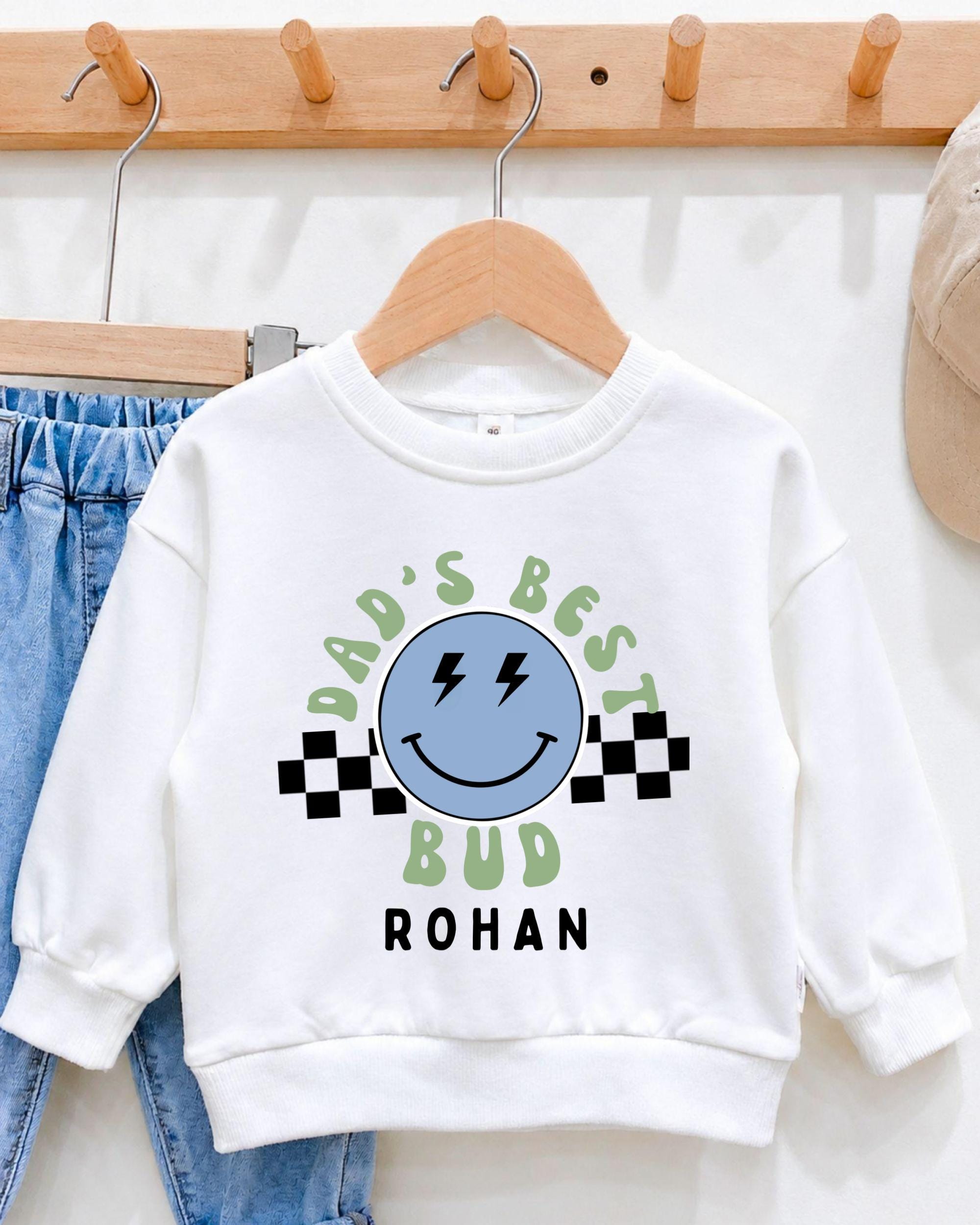 A white sweatshirt with a graphic design and text printed on it, hanging on a wooden hanger.