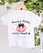 A white t-shirt with a graphic design featuring a pink pumpkin and the text "Mummy & Daddy's LITTLE PUMPKIN Olivia" printed on it.