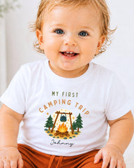A smiling baby wearing a white t-shirt with a camping-themed graphic and text.