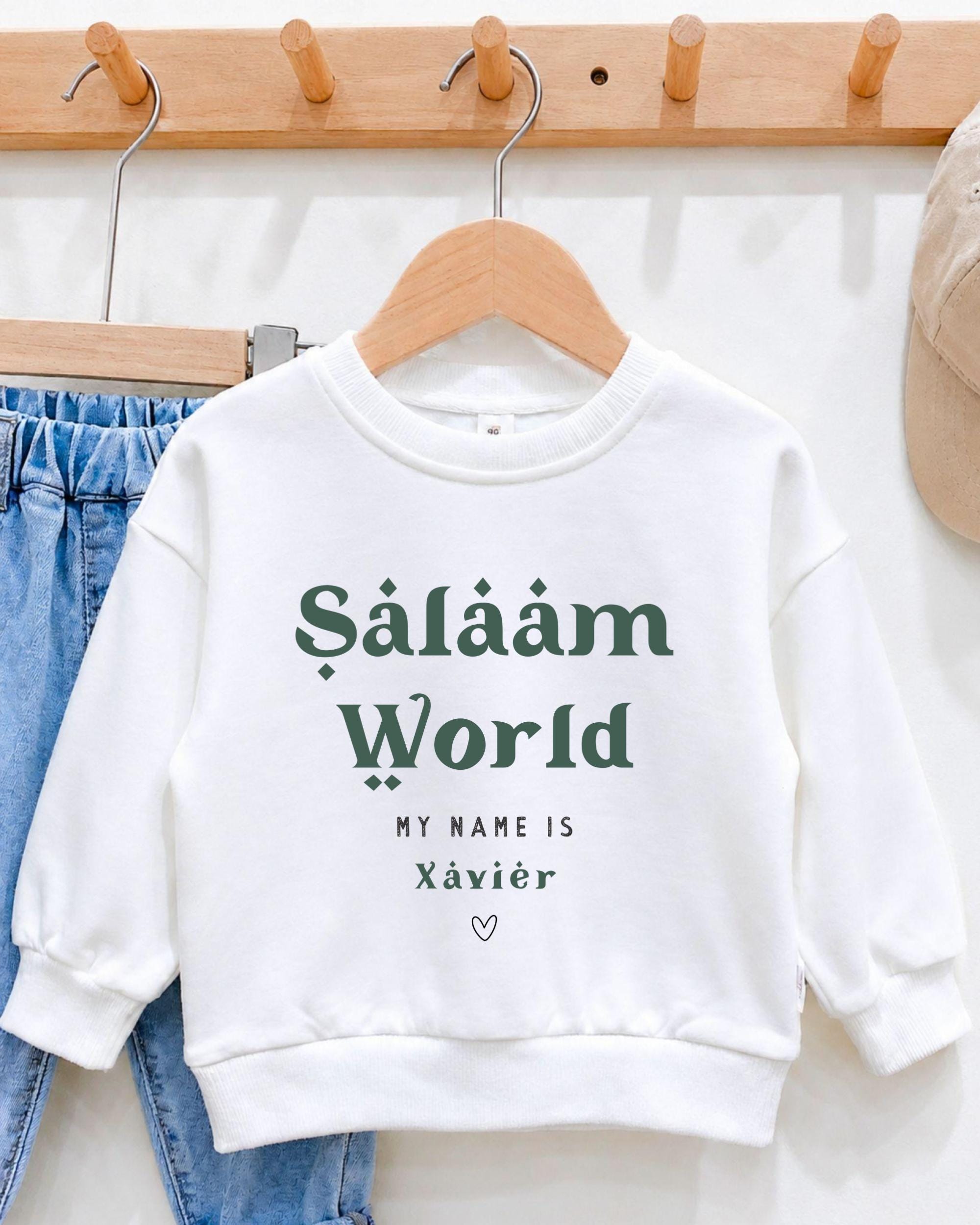 A white sweatshirt with the text "Saläm World" printed on it, hanging on a wooden hanger.
