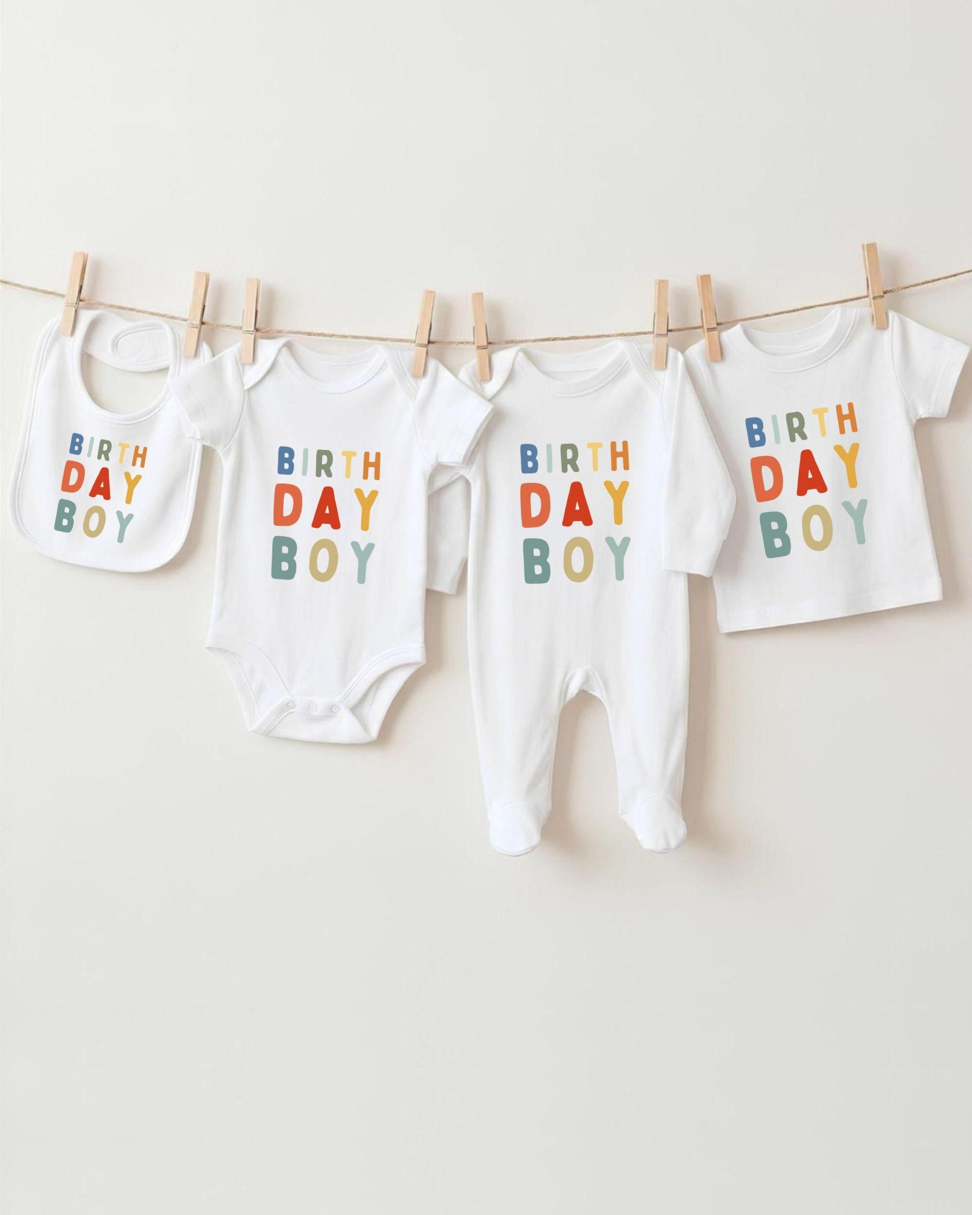 A collection of four white baby clothes, including onesies and bibs, hanging on a clothesline.