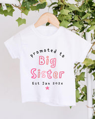 A white t-shirt with text that reads "Promoted to Big Sister Est Jan 202x" printed on it.