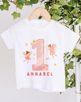 A white t-shirt with a pink number one and two-tailed fairy design, along with the text "Annabel" printed on it.