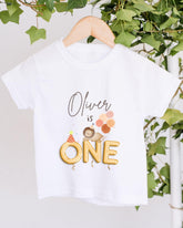 A white t-shirt with a personalized text and an illustration of a lion and balloons, hanging on a wooden hanger.