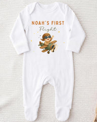 A white onesie with a cartoon image of a baby wearing a pilot's hat and flying an airplane, along with the text "Noah's first flight".