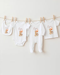 A collection of baby clothes, including onesies and bibs, hanging on a clothesline.