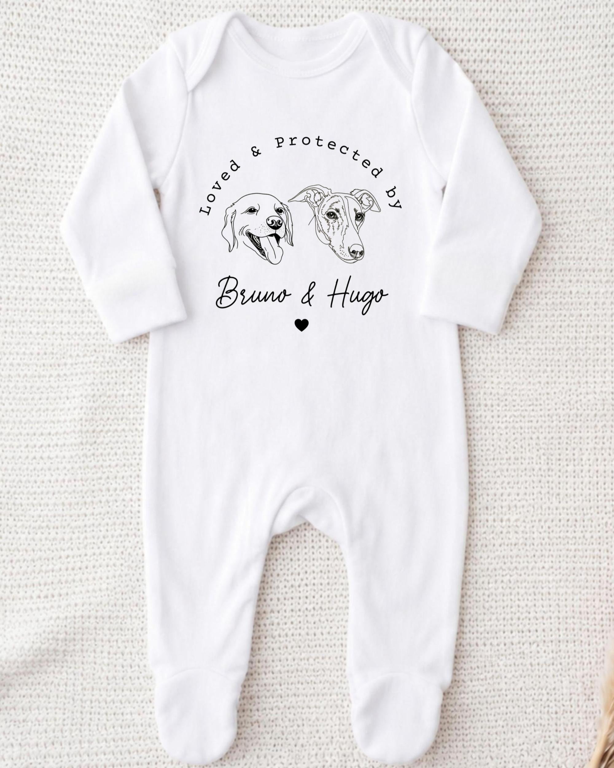 A white onesie with a graphic design featuring two dog heads and the text "Loved & Protected by Bruno & Hugo" printed on it.