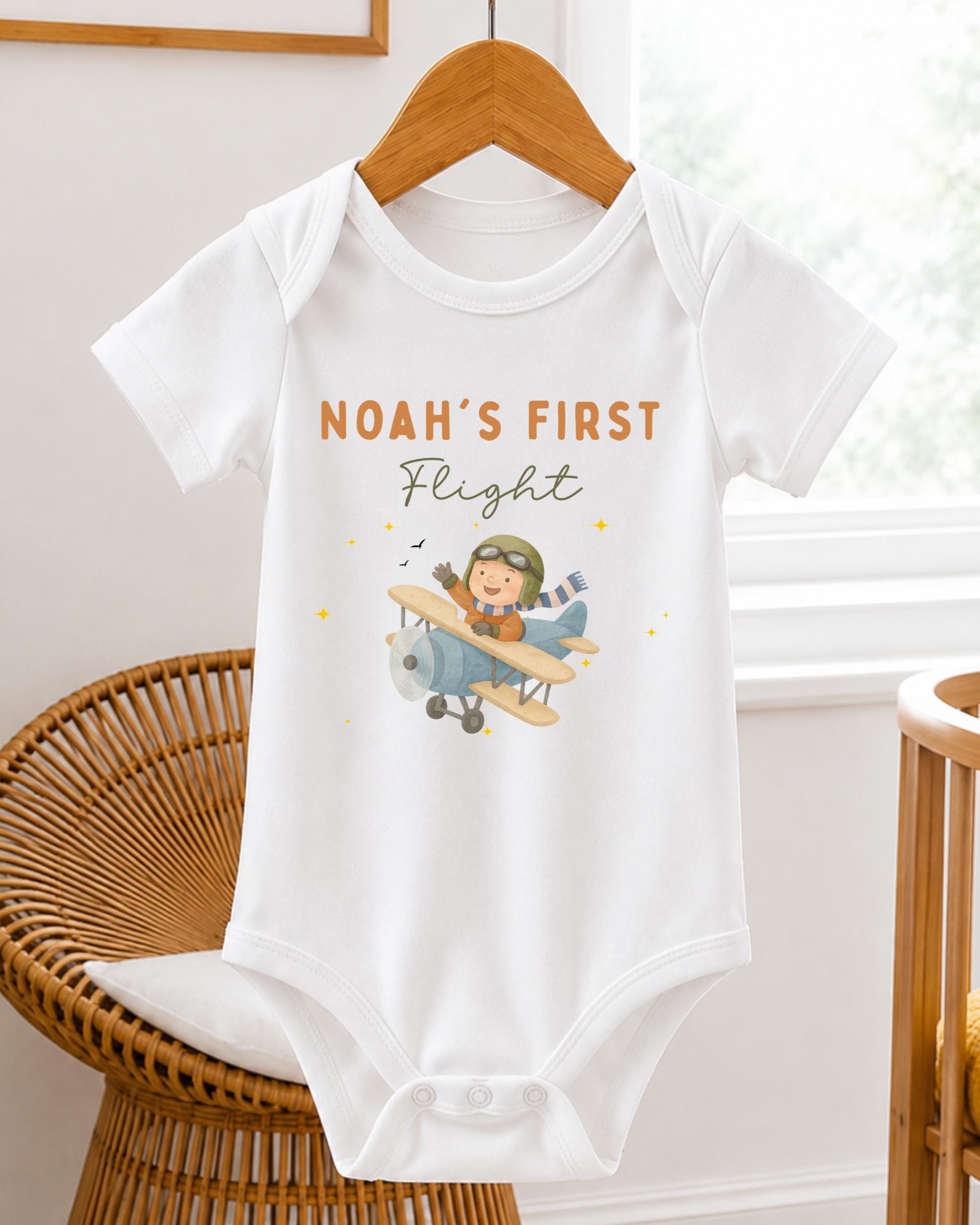 A white baby onesie with a cartoon airplane and the text "Noah's first flight" printed on it.