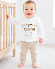 A smiling baby boy wearing a white sweatshirt with the text "Camping Crew Cornwall" and the date "July 2023" printed on it.
