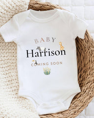 A white baby onesie with the text "BABY Harison COMING SOON" printed on it, along with illustrations of various animals.