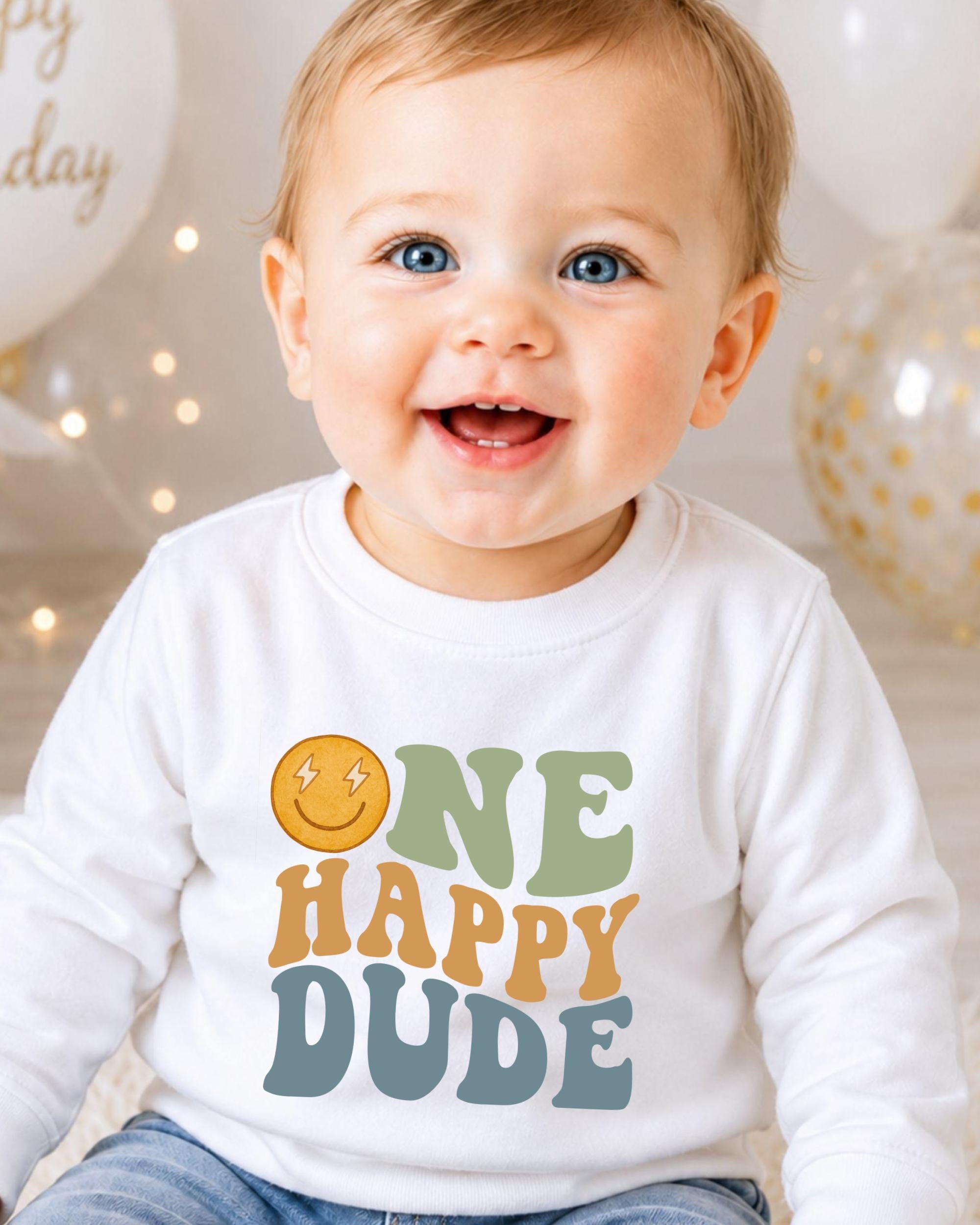 A smiling baby boy wearing a white shirt with a happy face and the text "ONE HAPPY DUDE" printed on it.