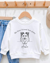 A white sweatshirt with a graphic of a dog's face and the text "My best friend has paws Archie" printed on it.