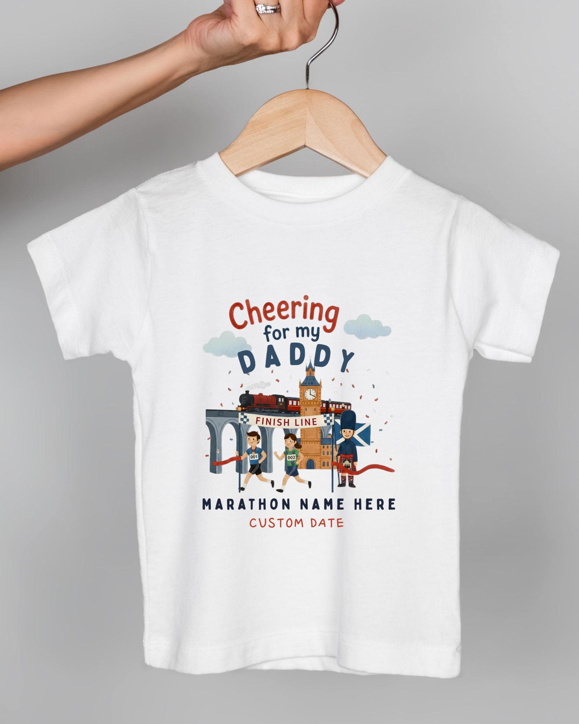 A white t-shirt with a graphic design depicting a race scene, including a finish line, runners, and a clock. The text on the t-shirt reads "Cheering for my DADDY" and "Marathon Name Here" along with "CUSTOM DATE".