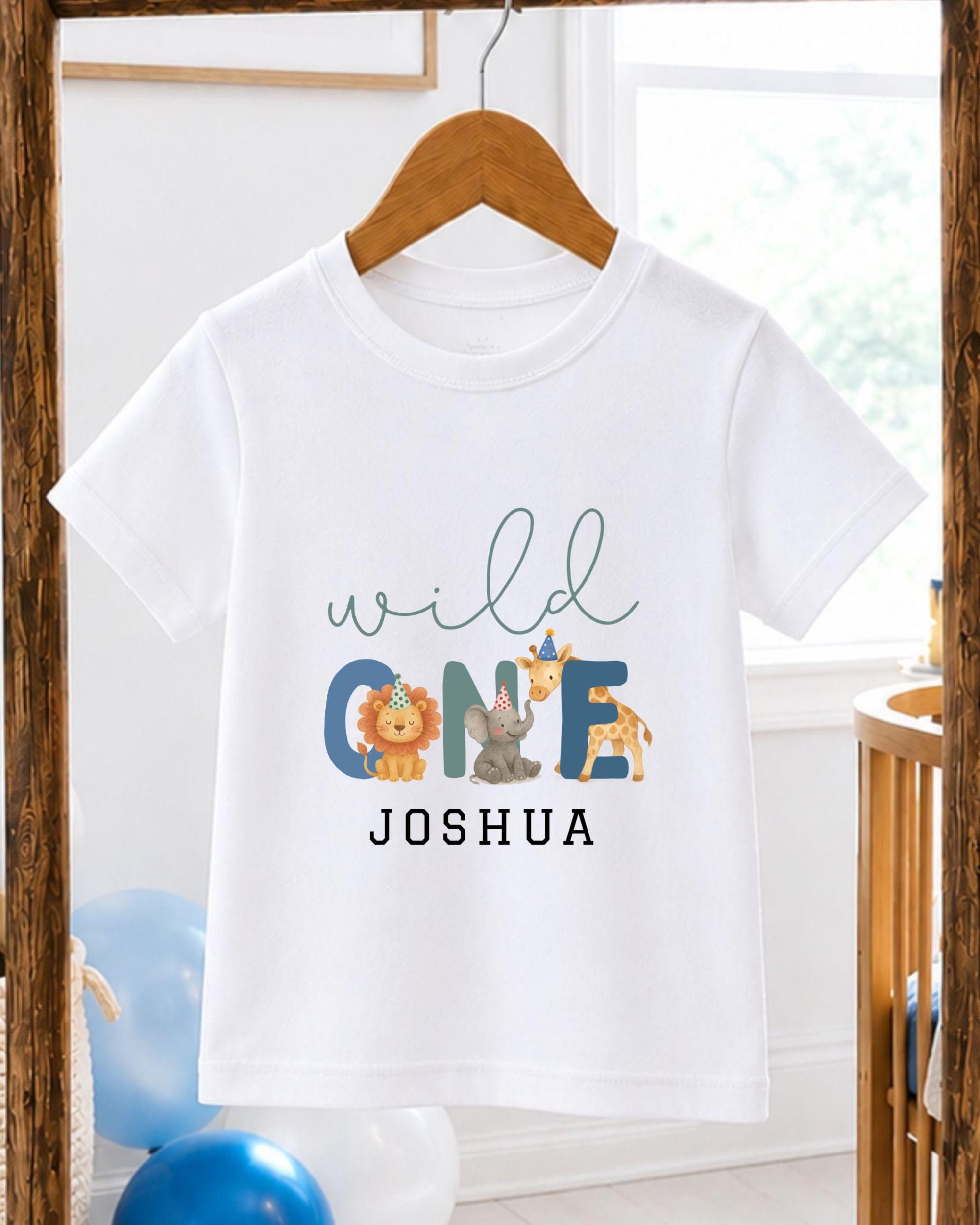 A white t-shirt with a personalized text and animal graphics printed on it, hanging on a wooden hanger.