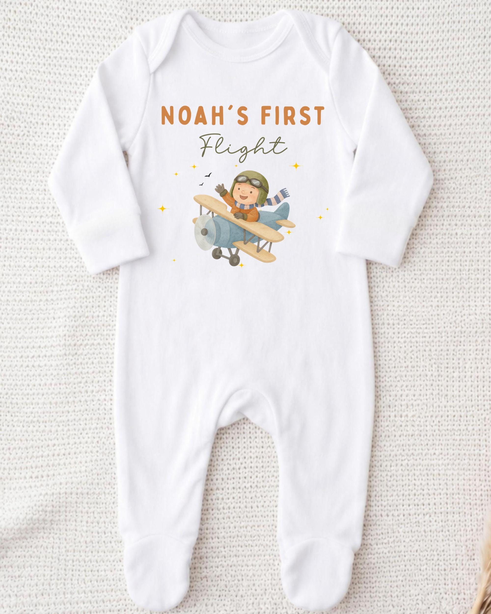 A white onesie with a cartoon airplane and the text "Noah's first flight" printed on it.