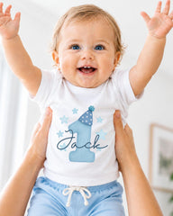 A smiling baby wearing a white onesie with a blue hat and stars, with the name "Jack" written on it.