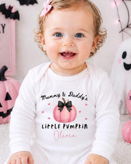 A smiling baby girl wearing a white onesie with a pumpkin design and text that says "Mummy & Daddy's Little Pumpkin Olivia".