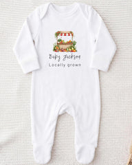 A white onesie with a printed design of a fruit stand and the text "Baby Jackson Locally grown" printed on it.