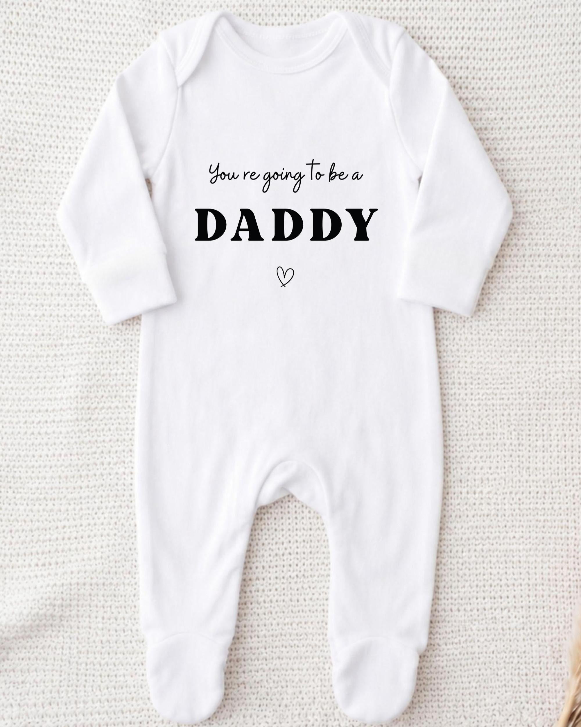 A white onesie with the text "You're going to be a DADDY" printed on it.