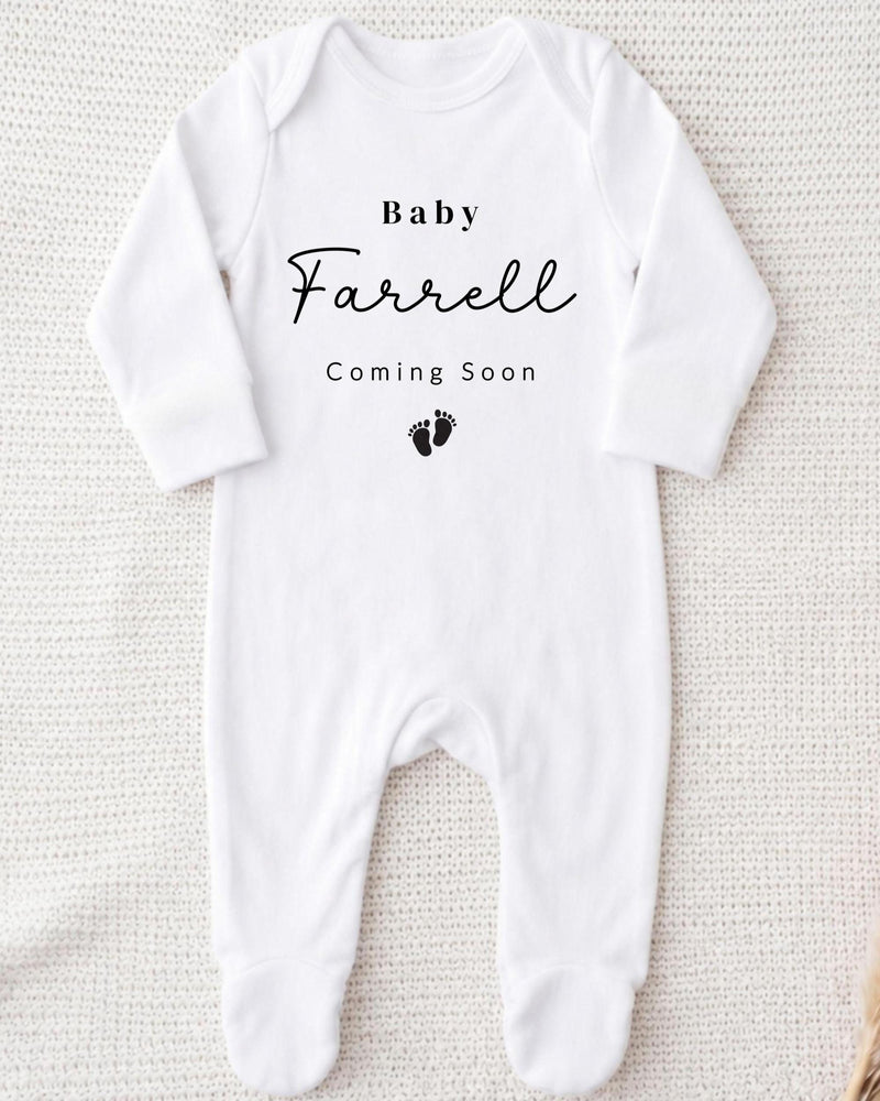 A white bodysuit with the text "Baby Farrell Coming Soon" printed on it.