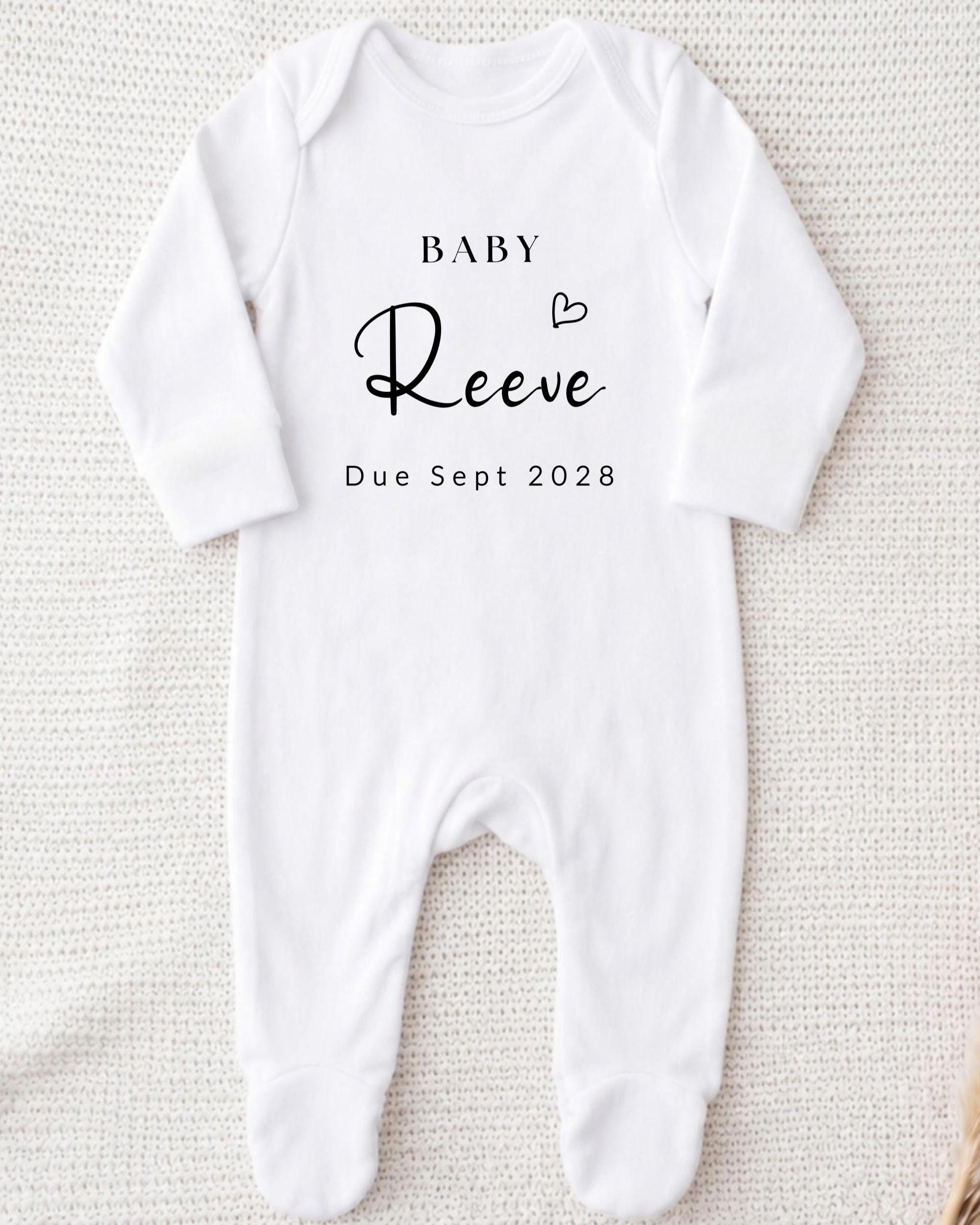 A white onesie with the text "BABY Reeve Due Sept 2028" printed on it.