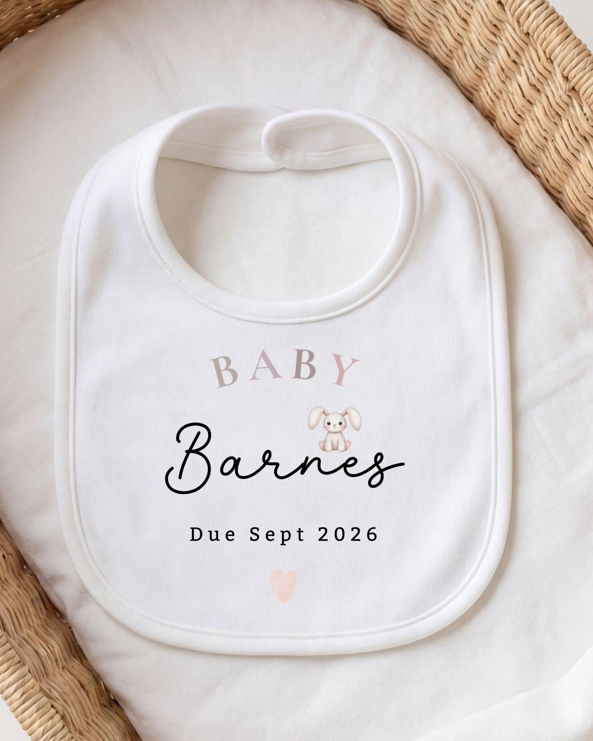 A white baby bib with the text "BABY Barnes Due Sept 2026" printed on it, placed on a white cloth.